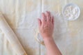 WomanÃ¢â¬â¢s hand dropping flour on ball of cookie dough, pastry cloth, wood rolling pin with cloth cover, small bowl of flour